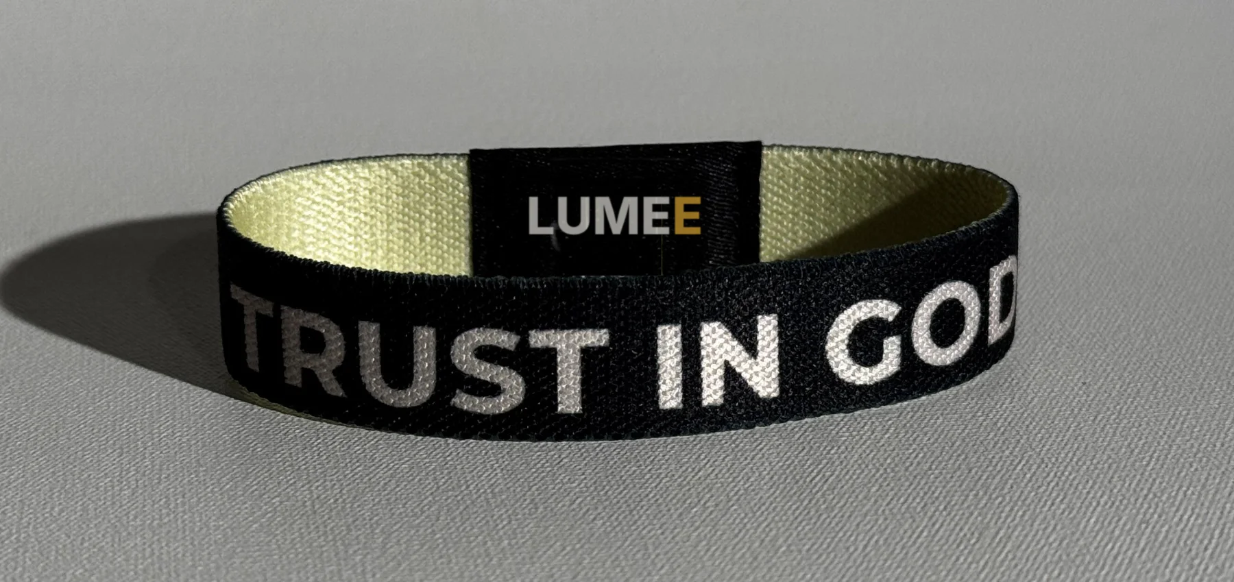 Schwarzes LUMEE-Band mit der Aufschrift Trust in God und dem LUMEE-Patch, innen crème